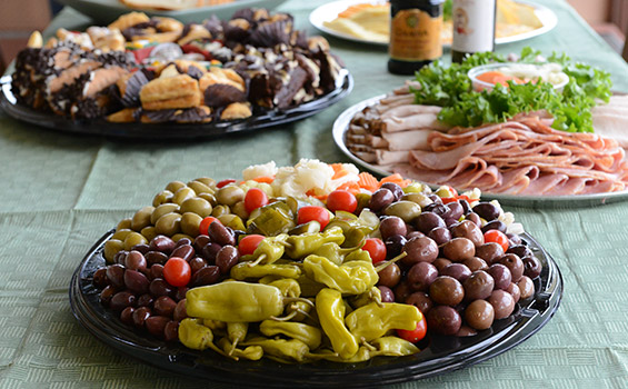 A few party trays on a table: Deli meats, olives, cheeses