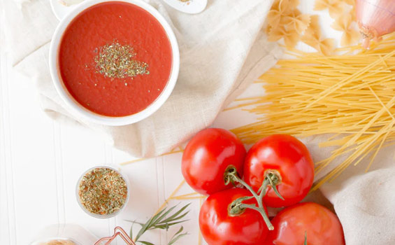 Sauce in a bowl with fresh tomatoes and dry pasta on a table